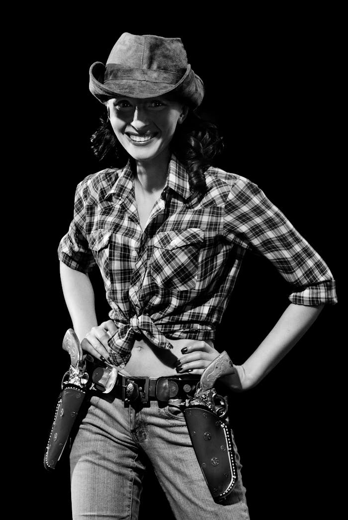 services-03 Black and white portrait of a smiling cowgirl in a plaid shirt and hat.